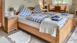 A cozy bedroom with a wooden bed, checkered pillows, a bedside table with a lamp, and a wall clock.