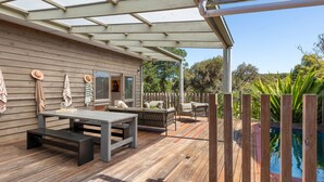 En træterrasse med pool, havemøbler og et pergola.