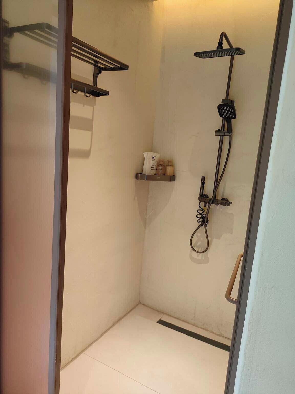 A small, enclosed shower area with a handheld showerhead, a towel rack, and a shelf with toiletries.