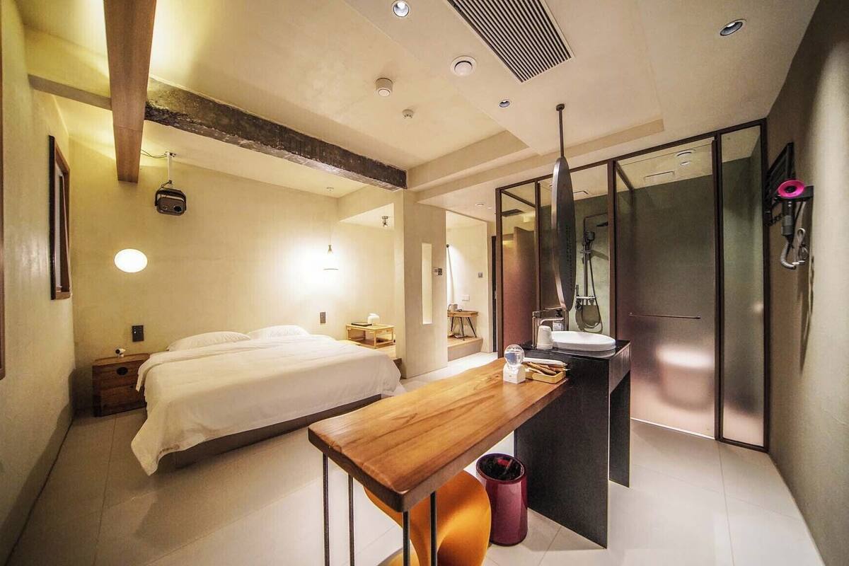 Ein modernes Hotelzimmer mit Bett, Nachttisch und einem Badezimmer mit Spiegel und Waschbecken.