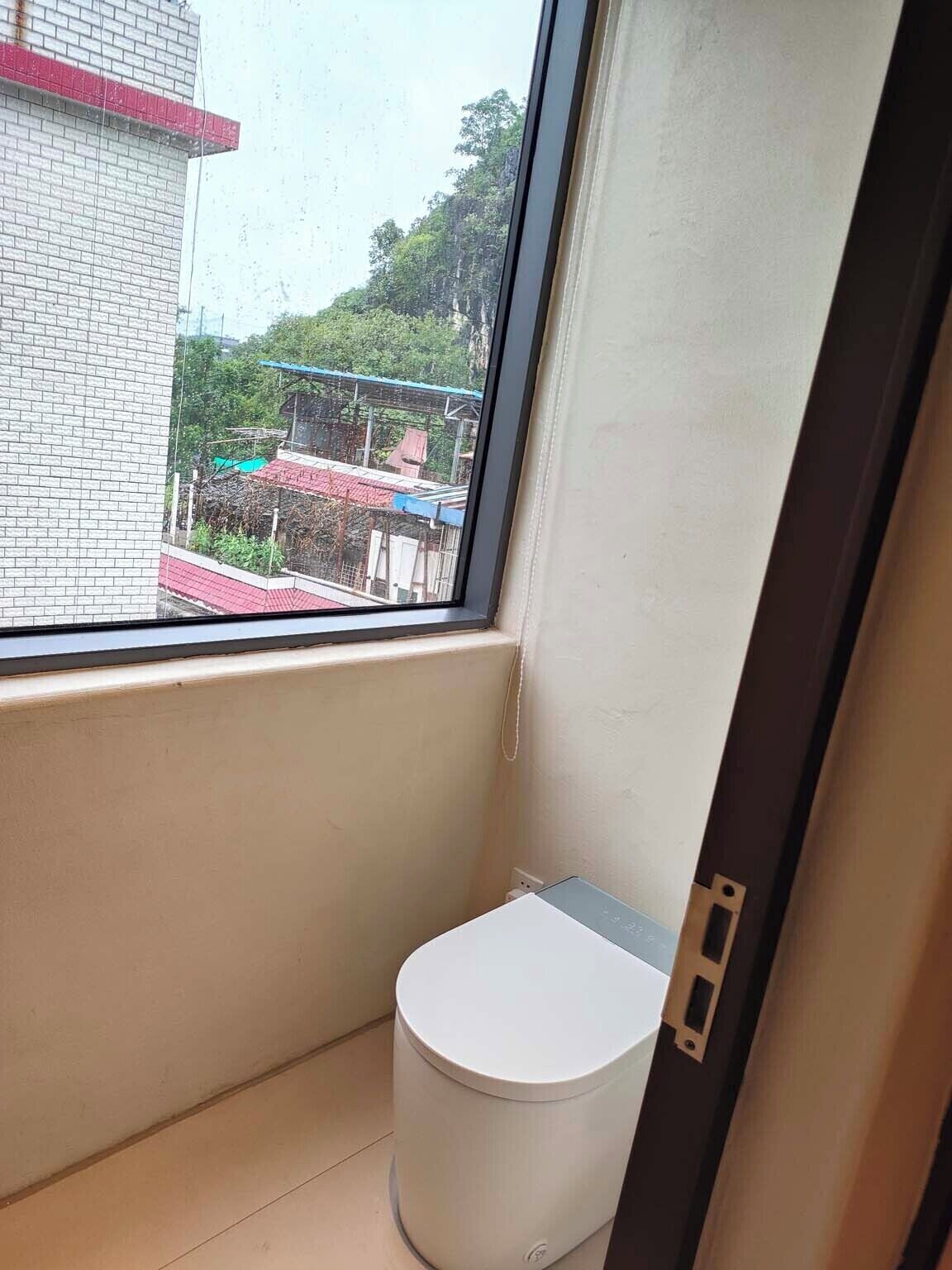 Un baño pequeño con inodoro, ventana y vistas a edificios.