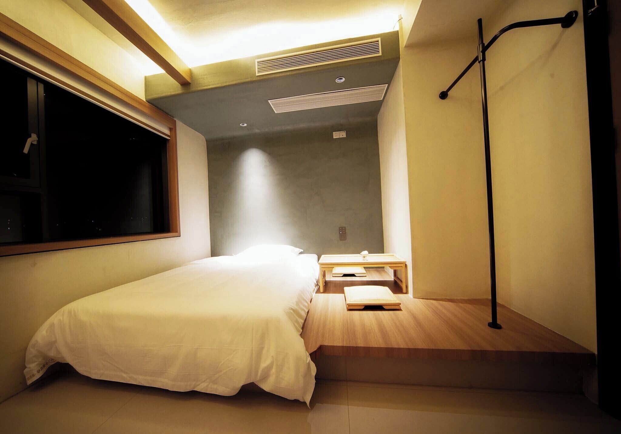 A compact bedroom with a bed, a nightstand, a small table, and a window.