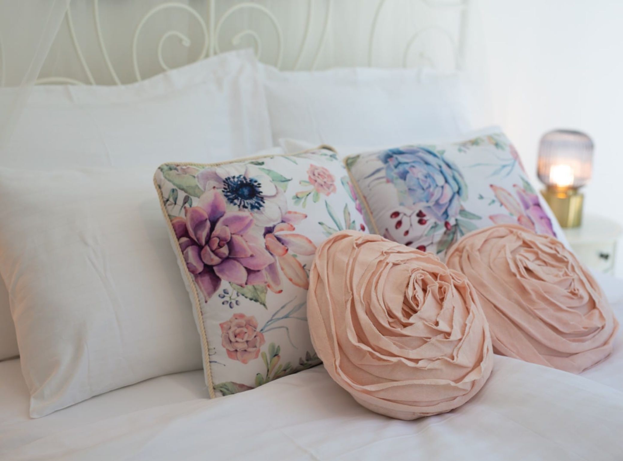 A bed with white linens, floral-patterned pillows, and a decorative headboard.