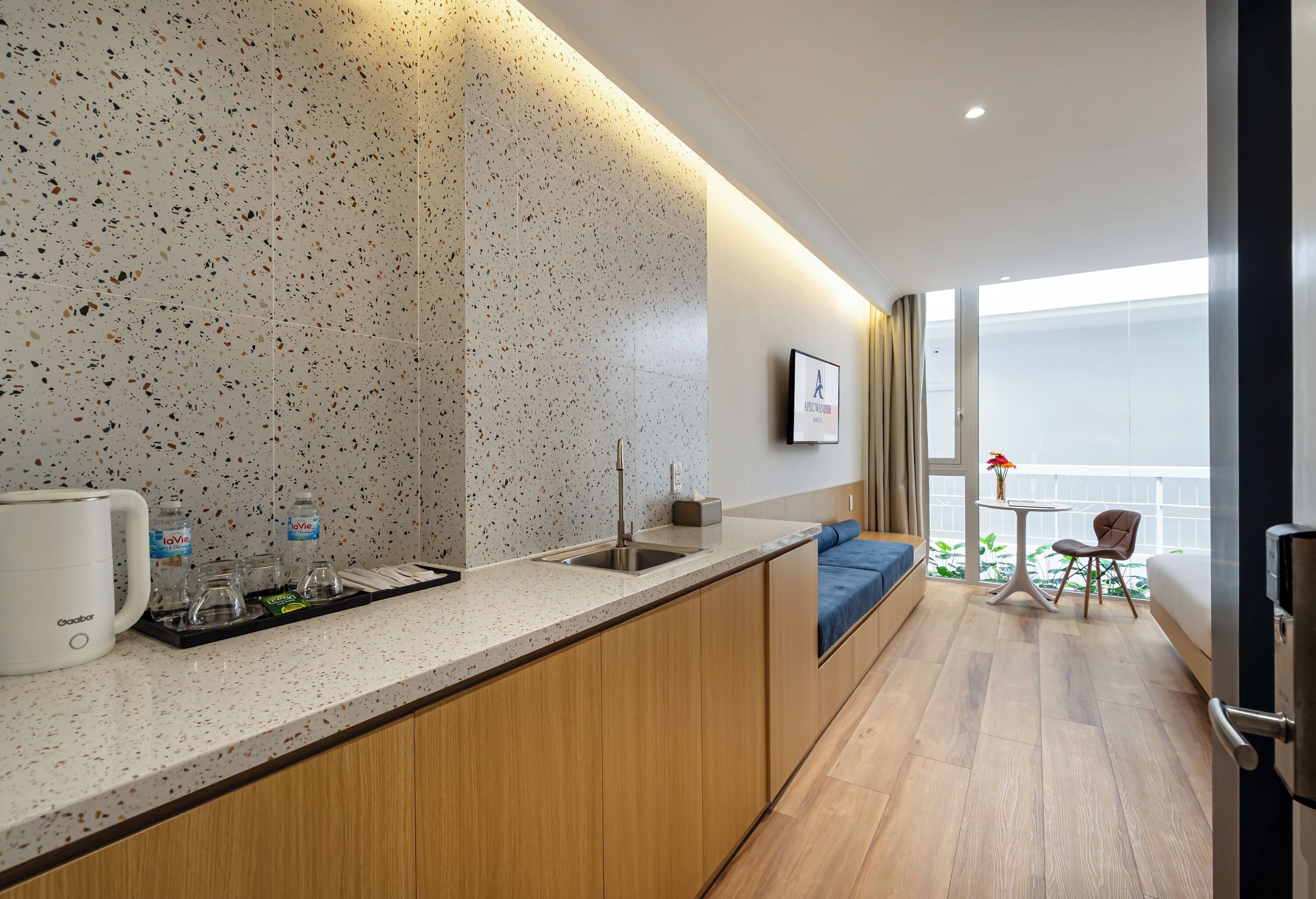 A modern kitchen with a speckled backsplash, a coffee maker, and a tray with glasses and a bottle.