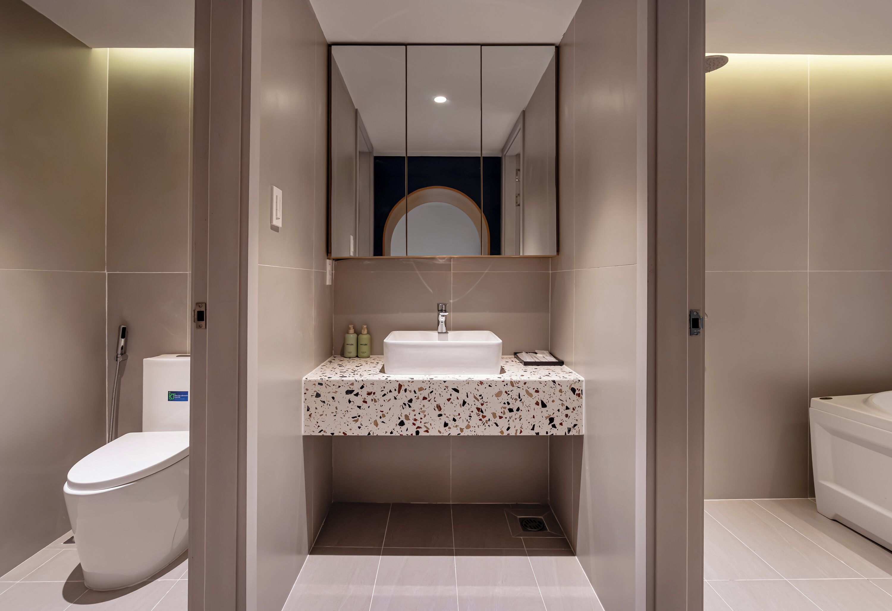 Een moderne badkamer met een wit toilet, een wastafel met een gevlekt aanrechtblad en een spiegel boven de wastafel.