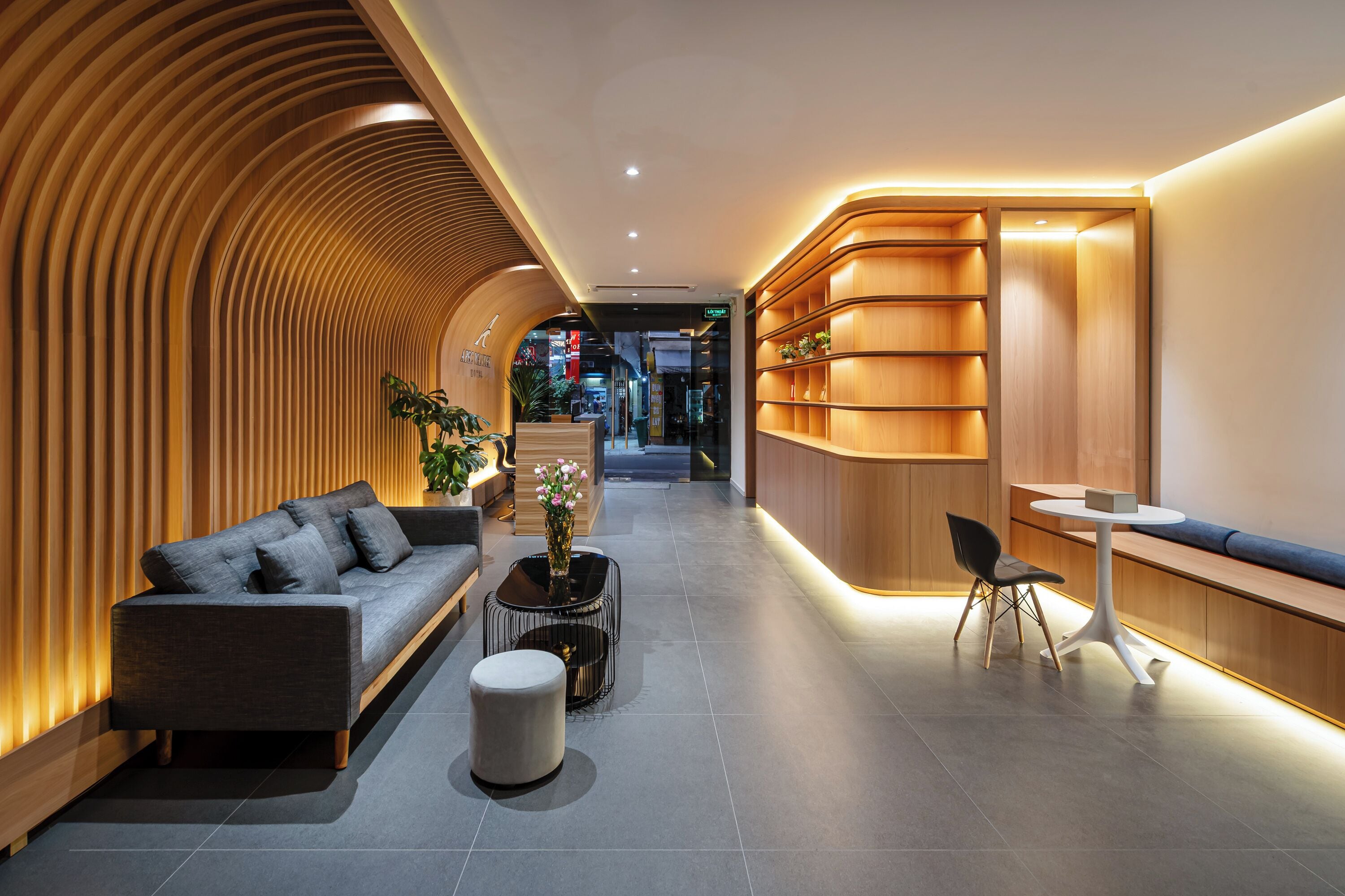 Un hall d’entrée moderne avec un mur en bois incurvé, un canapé, une table basse, une petite table ronde et un espace détente avec un banc.
