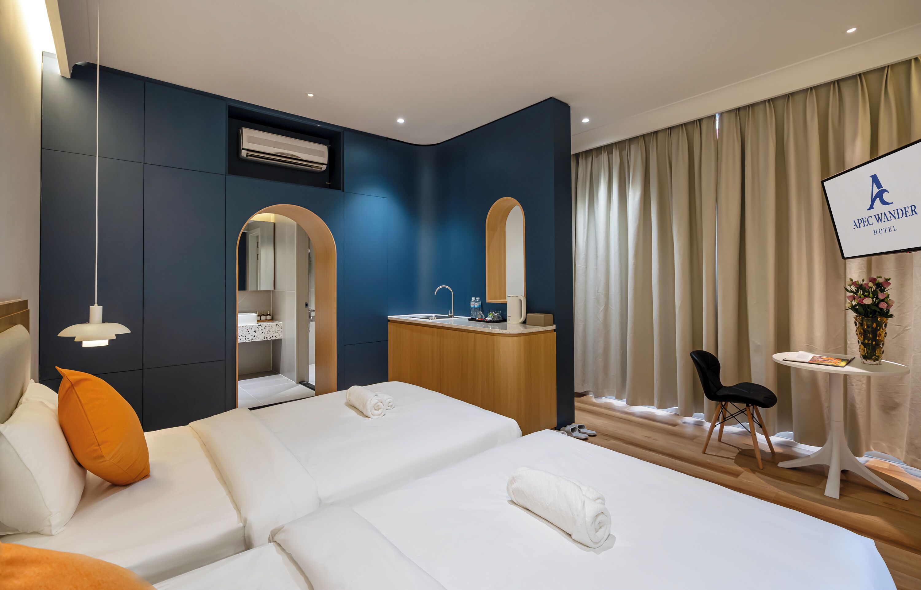 A hotel room with two beds, a desk, a mirror, a TV, and a window with curtains.