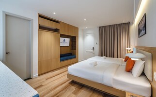 A hotel room with a bed, a seating area with a blue cushion, a wardrobe, and a sign indicating the hotel name.