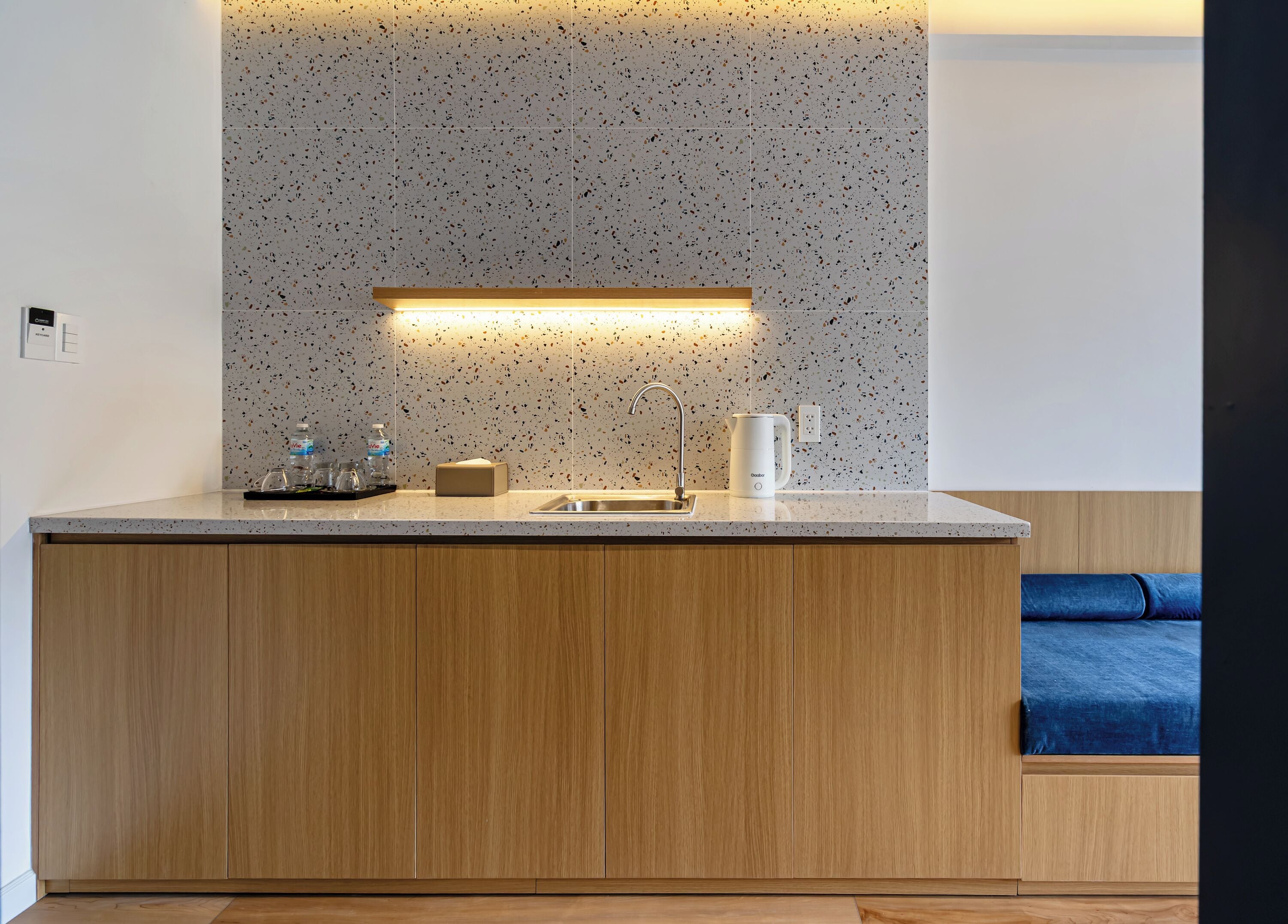 Una cocina moderna con salpicadero moteado, armarios de madera, un lavamanos de acero inoxidable y una cafetera integrada.