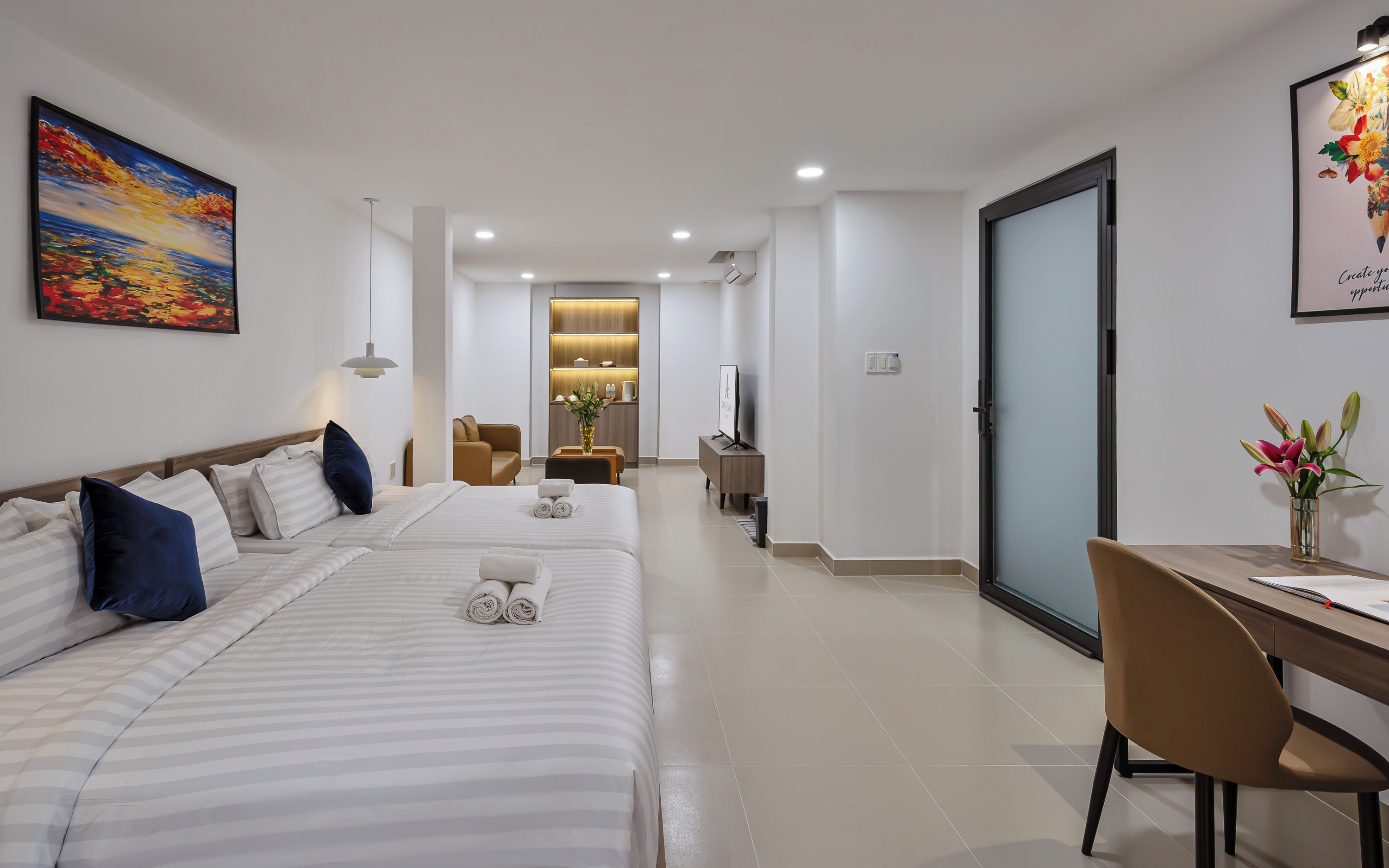 Habitación de hotel con dos camas, un escritorio, una silla, un televisor y un baño al fondo.