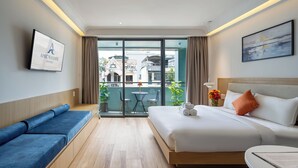 Een hotelkamer met een bed, een bank, een bureau en uitzicht op de stad door grote ramen.