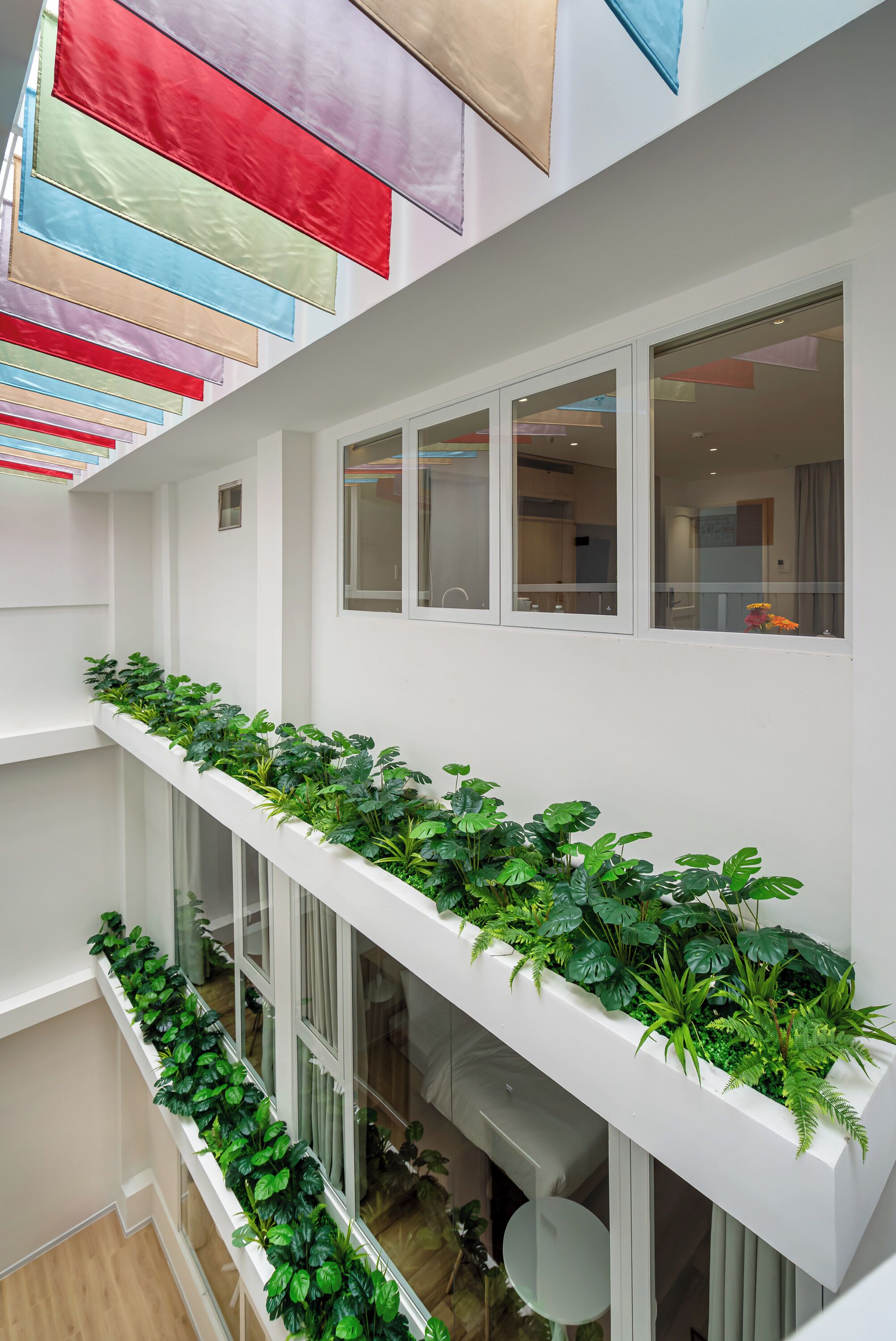 A multi-level interior with a balcony adorned with green plants, white walls, and large windows.