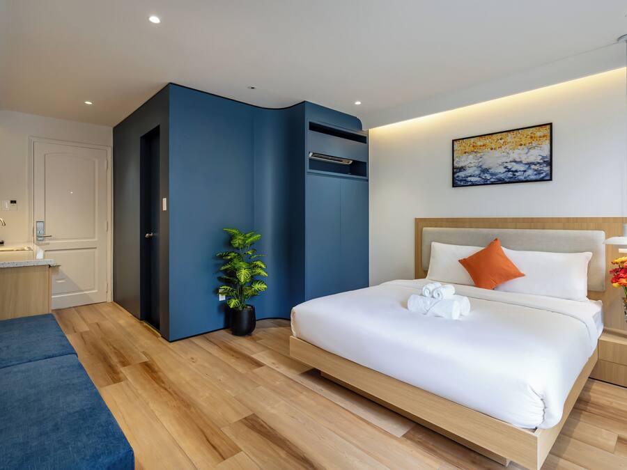 A modern hotel room with a large bed, a desk, a blue accent wall, and a potted plant.