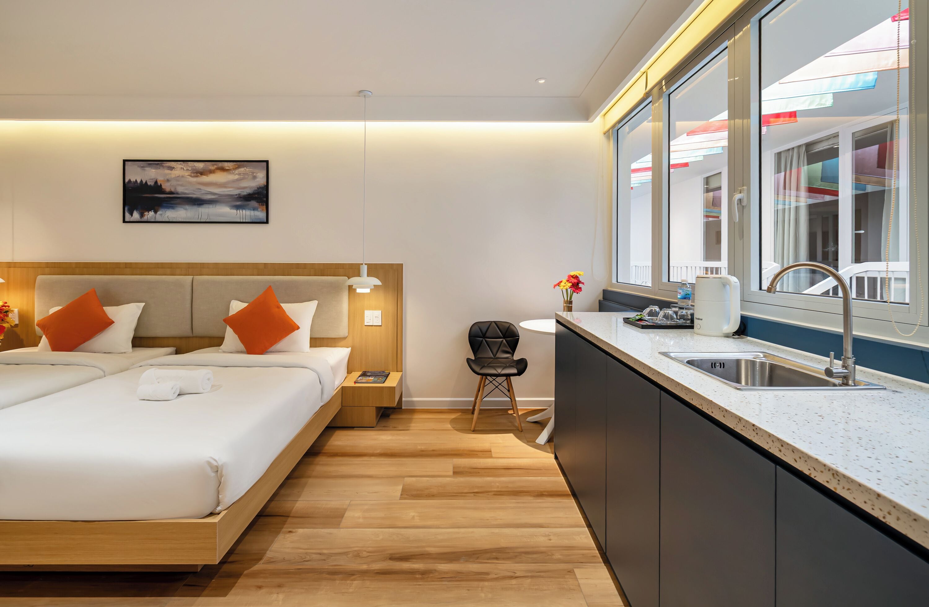 Une chambre d’hôtel moderne dotée d’un grand lit, de tables de chevet, d’un petit coin cuisine et d’une fenêtre donnant sur l’extérieur.