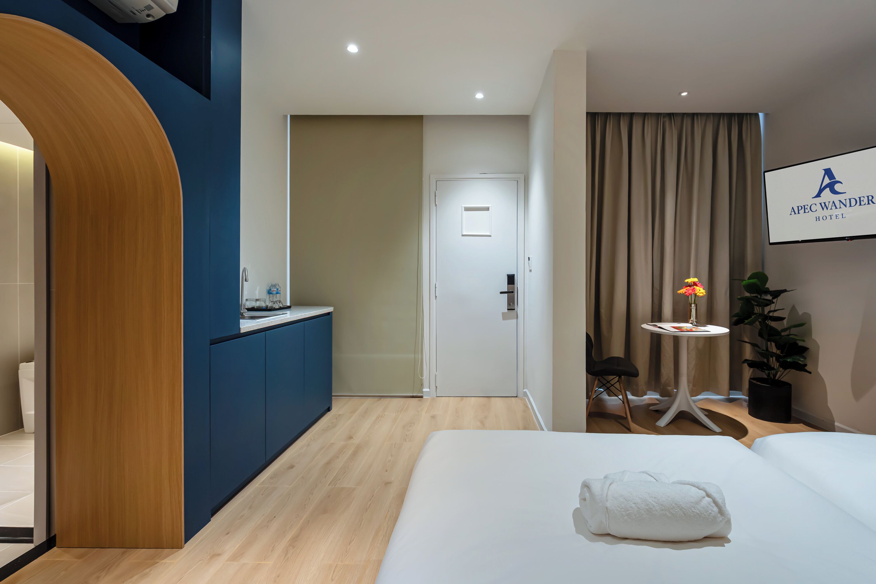 Ein Hotelzimmer mit einem Bett, einem kleinen Tisch mit einer Vase, einer Topfpflanze und einem Schild mit der Aufschrift APEC WANDER HOTEL.