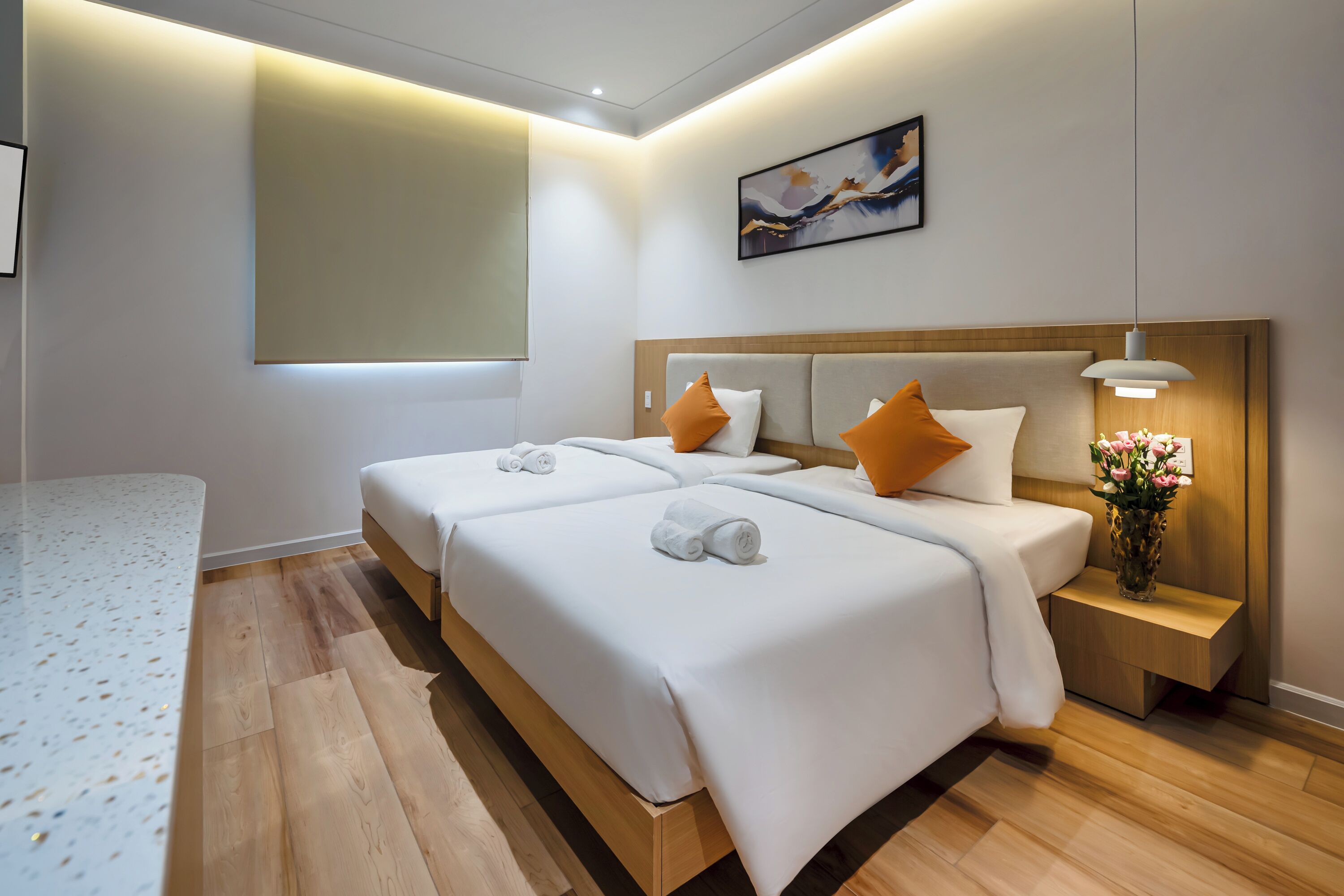 A hotel room with two beds, a bedside table with a lamp, and a painting on the wall.