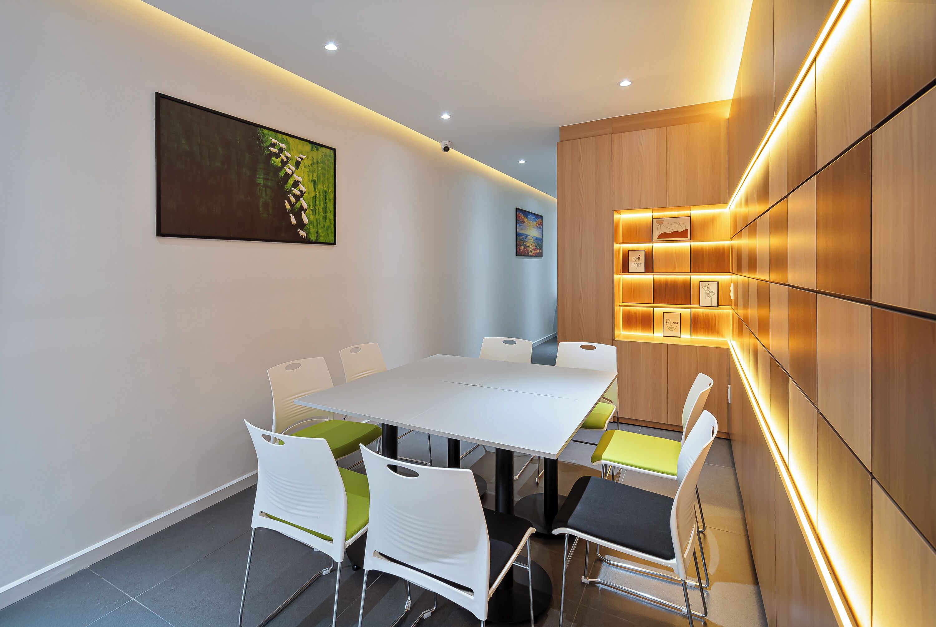 Una sala de reuniones moderna con una mesa y sillas blancas, y una pared de acento de madera con paneles iluminados.