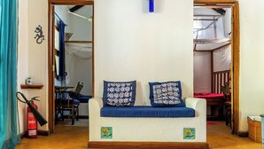 A living room with a sofa, patterned cushions, a fire extinguisher, a patterned rug, and a small decorative item on the wall.