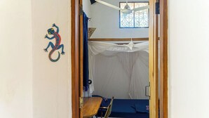 A room with a bed, a chair, a mosquito net, and a decorative lizard on the wall.