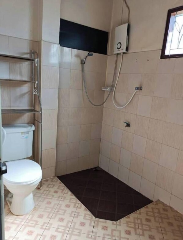 Une petite salle de bain comprenant des toilettes, une douche et une étagère.