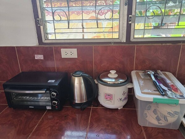 Una cocina con un horno tostador negro, un hervidor de acero inoxidable, una olla de cocción lenta blanca y un recipiente de plástico con un diseño floral.