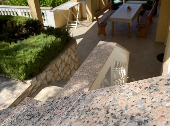 Eine Steinsäule, ein kleiner Garten und eine Terrasse mit Tisch und Bänken.