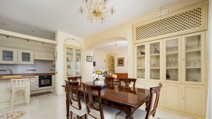 Un comedor con una mesa y sillas de madera, una araña, y una cocina al fondo.