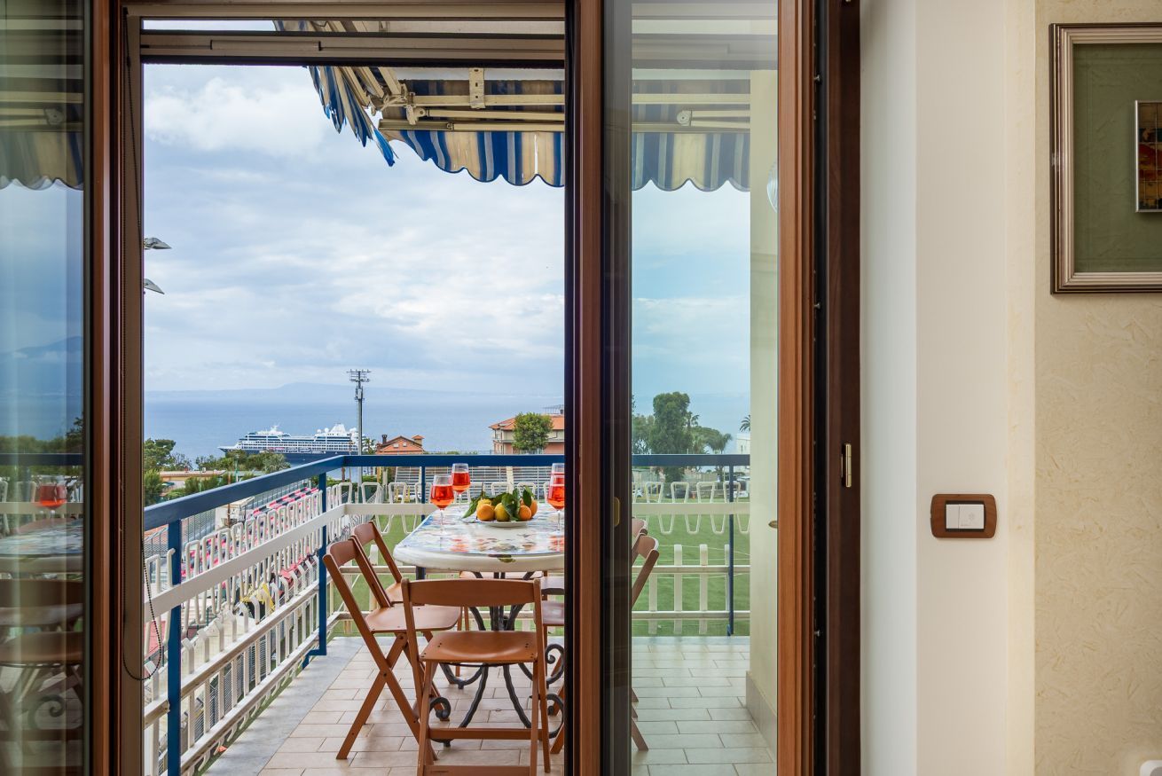 A balcony with a table set for two, a railing, and a view of the sea and buildings.