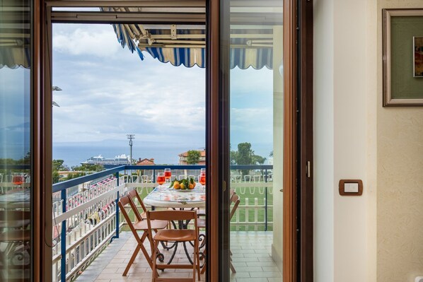 Een balkon met een tafel voor twee personen, een leuning en uitzicht op zee en gebouwen.