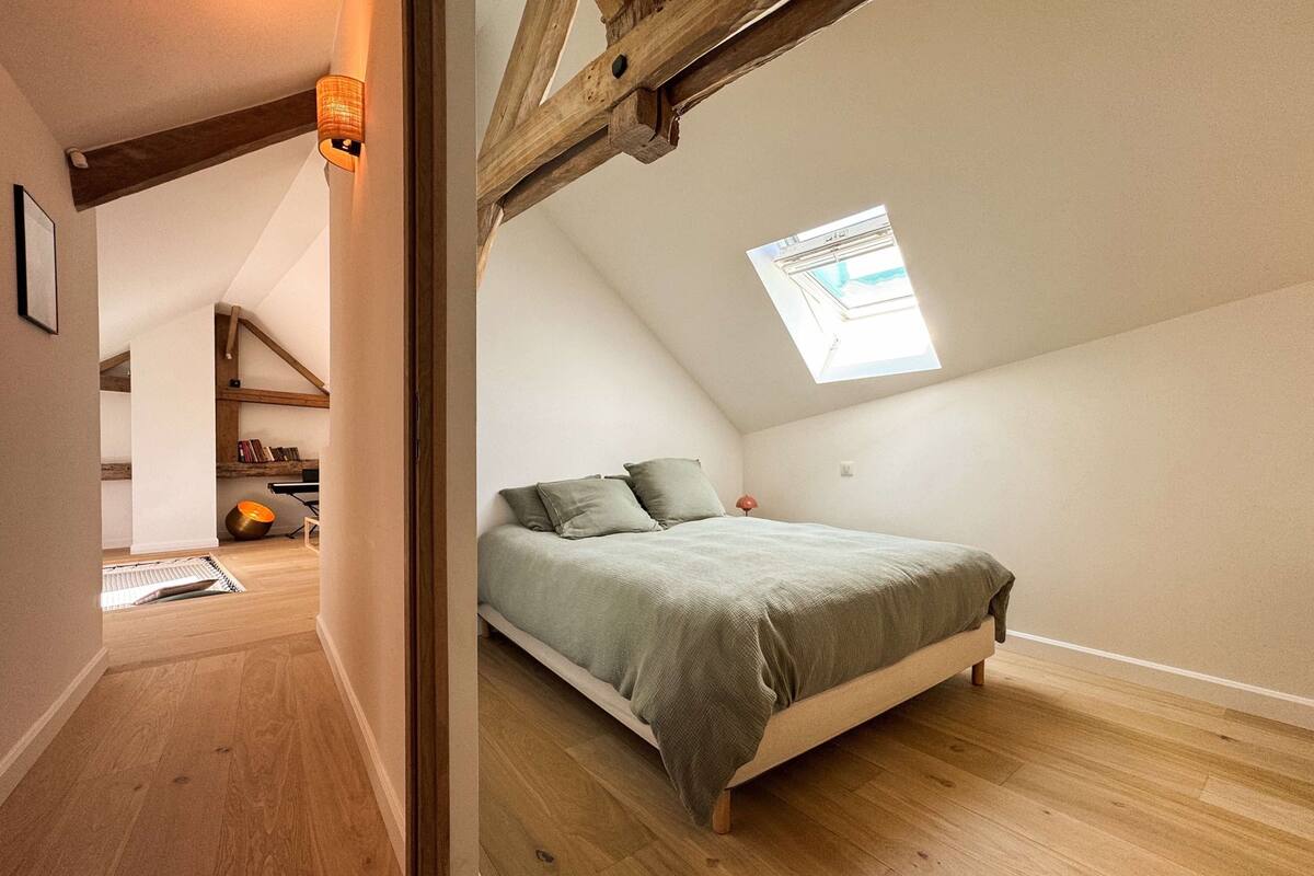 A bedroom with a sloped ceiling, a skylight, a bed, and a wooden floor.