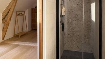 A modern shower with a glass door, wooden beams, and a tiled floor.