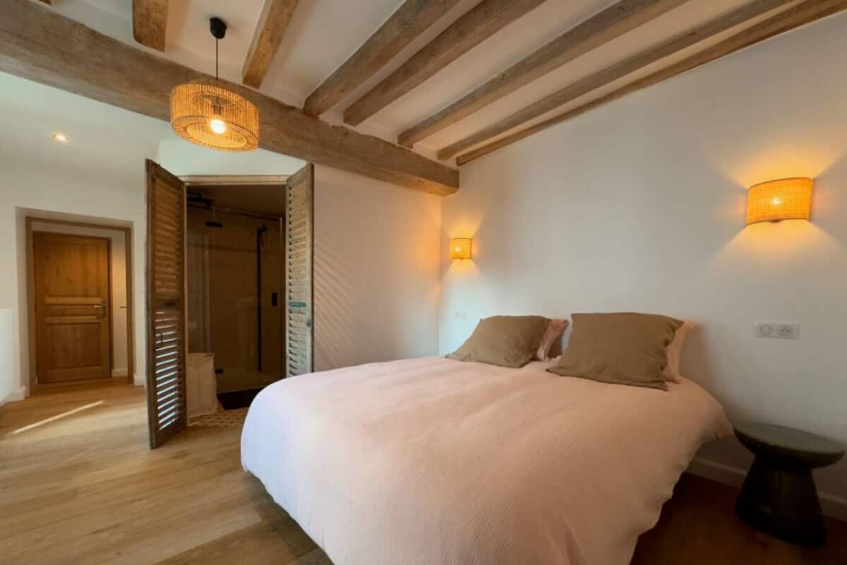 A bedroom with a large bed, wooden beams, a hanging light fixture, and two wall-mounted lights.