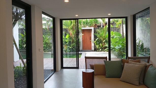 Un salon moderne avec un canapé, une table basse et une vue sur un jardin luxuriant, visible à travers de grandes portes-fenêtres coulissantes.