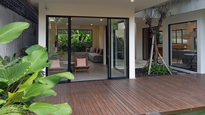 Une maison moderne dotée d’une terrasse en bois et de portes-fenêtres coulissantes qui donnent sur un espace de vie comprenant un canapé et une table à manger.