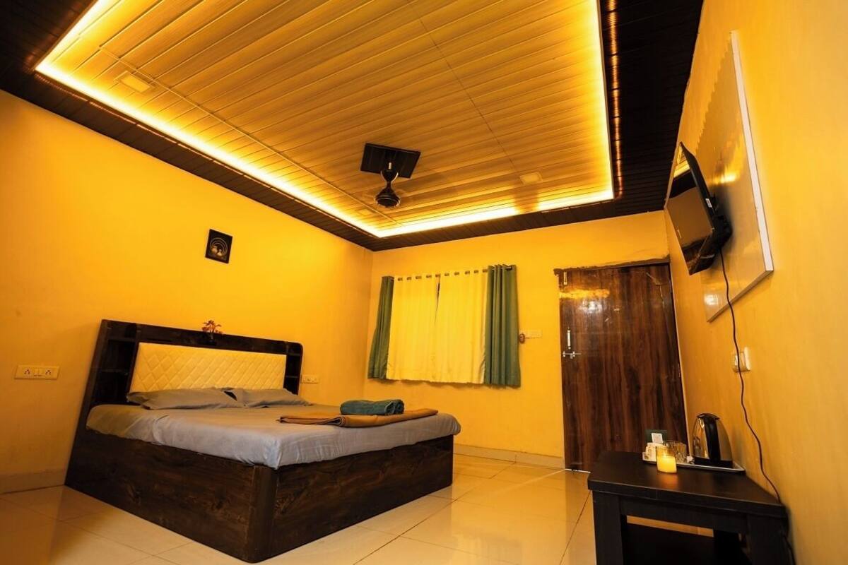 A bedroom with a bed, a ceiling fan, a TV mounted on the wall, and a small table with a candle.