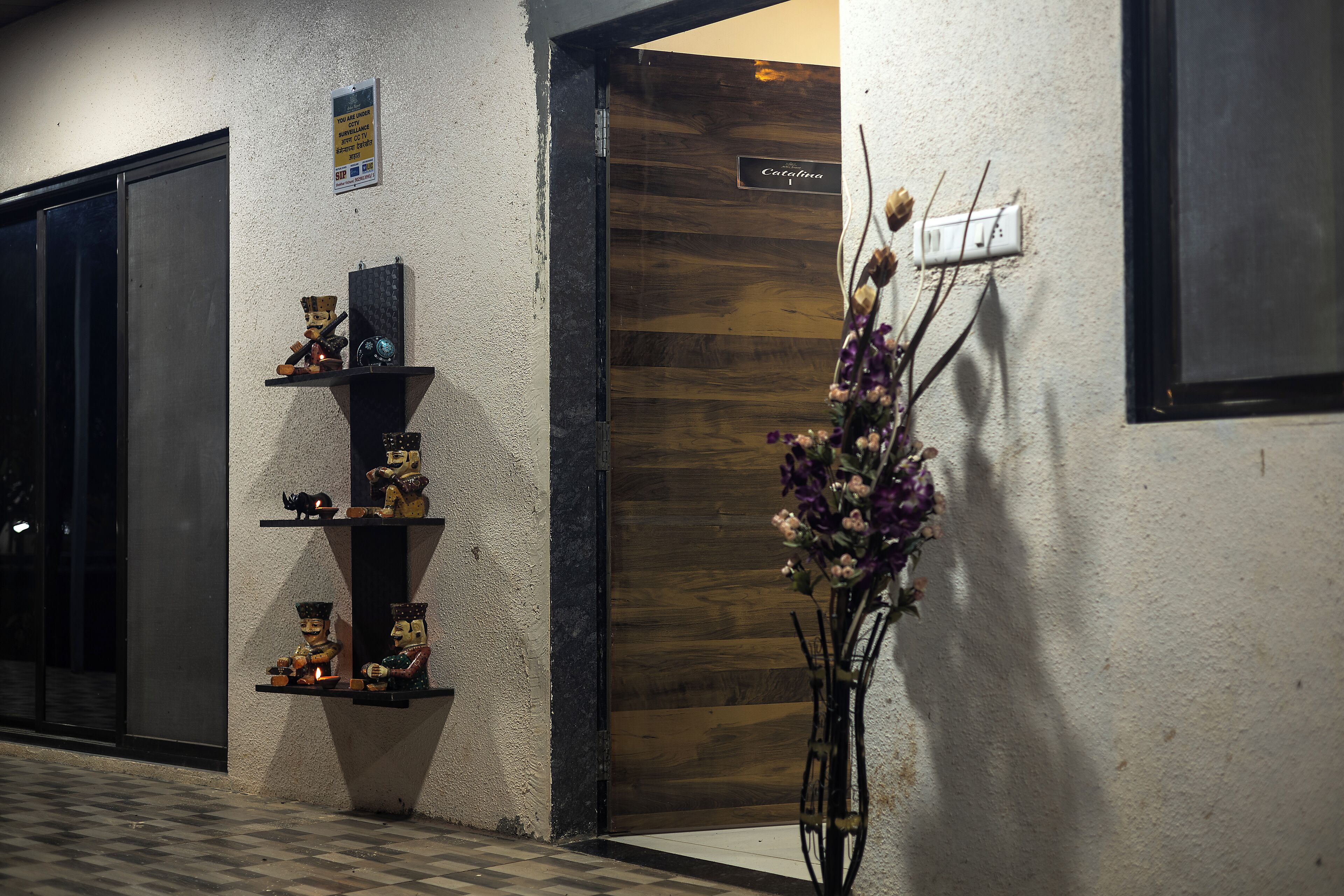 A hotel entrance with a wooden door, a wall-mounted sign, and a decorative shelf with figurines.