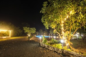 A nighttime outdoor area with a swimming pool, surrounded by trees and illuminated by string lights. - Arbor Resort (Karjat)