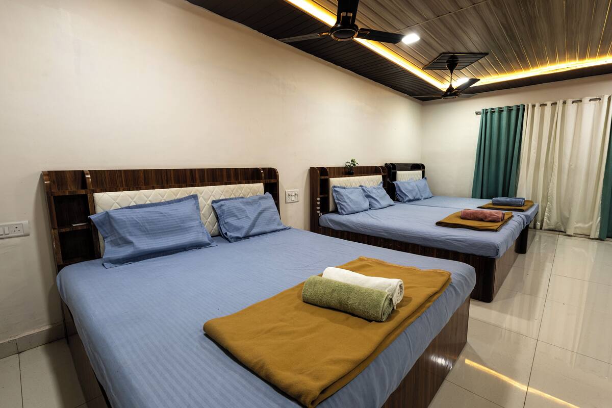 A hotel room with two beds, each with a wooden headboard, blue bedding, and a brown throw blanket.