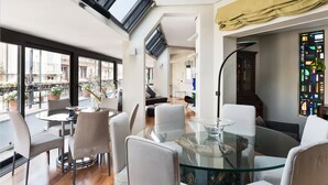 Un interior moderno con una mesa de vidrio, sillas blancas, un sofá y un ventanal de vitrales.