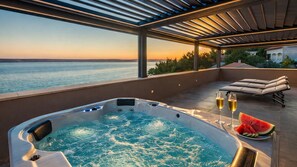 Un bain Ă remous avec vue sur la mer, des chaises longues et une coupe de champagne.