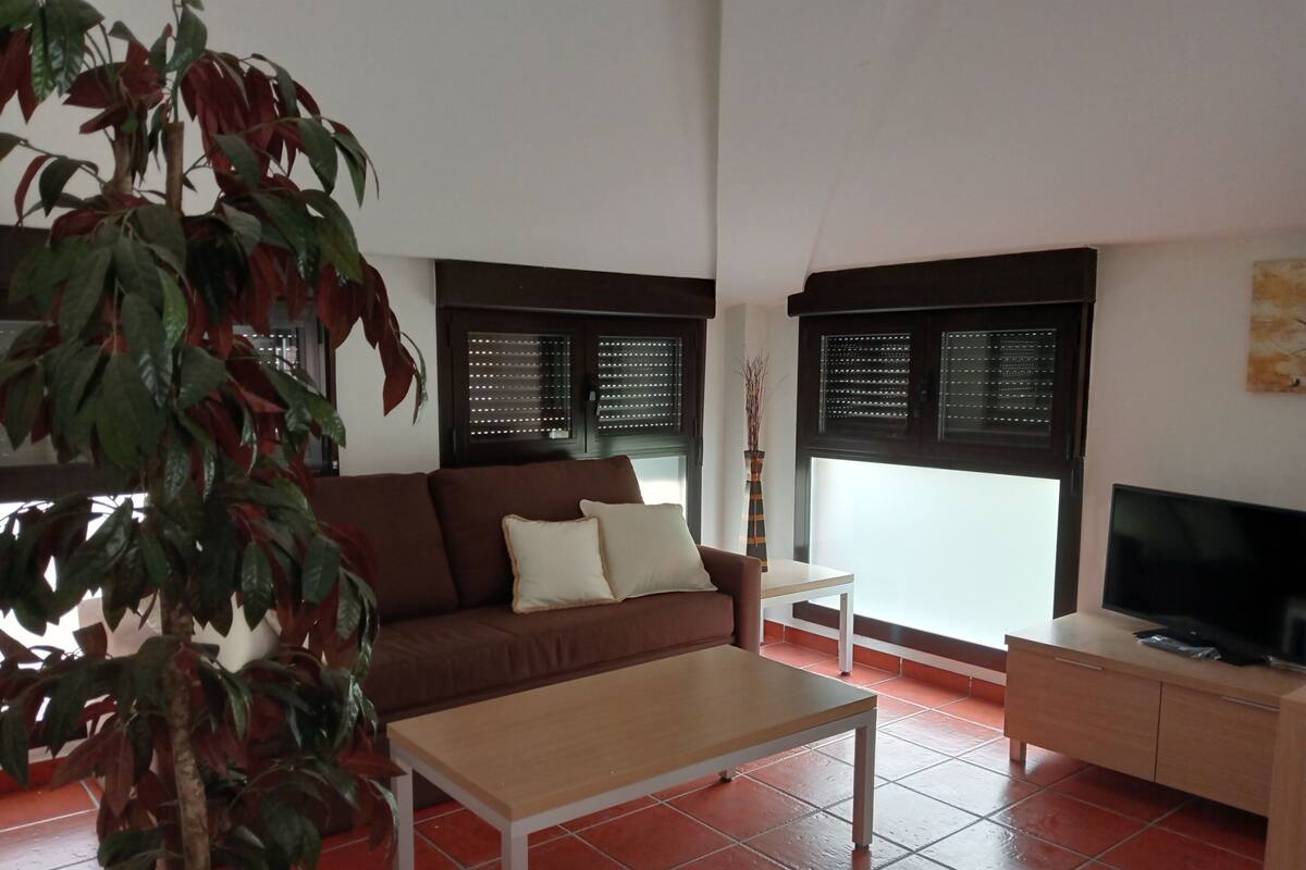 Een woonkamer met een bruine bank, een witte salontafel, een tv-meubel en een potplant.
