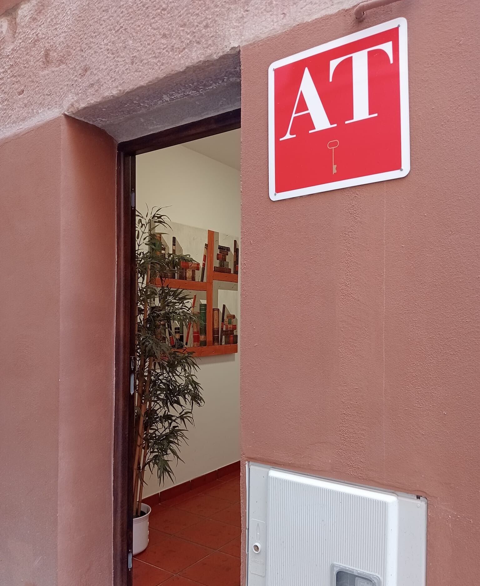 Une porte avec une enseigne rouge sur laquelle on peut lire « AT », et une plante en pot à l’intérieur.