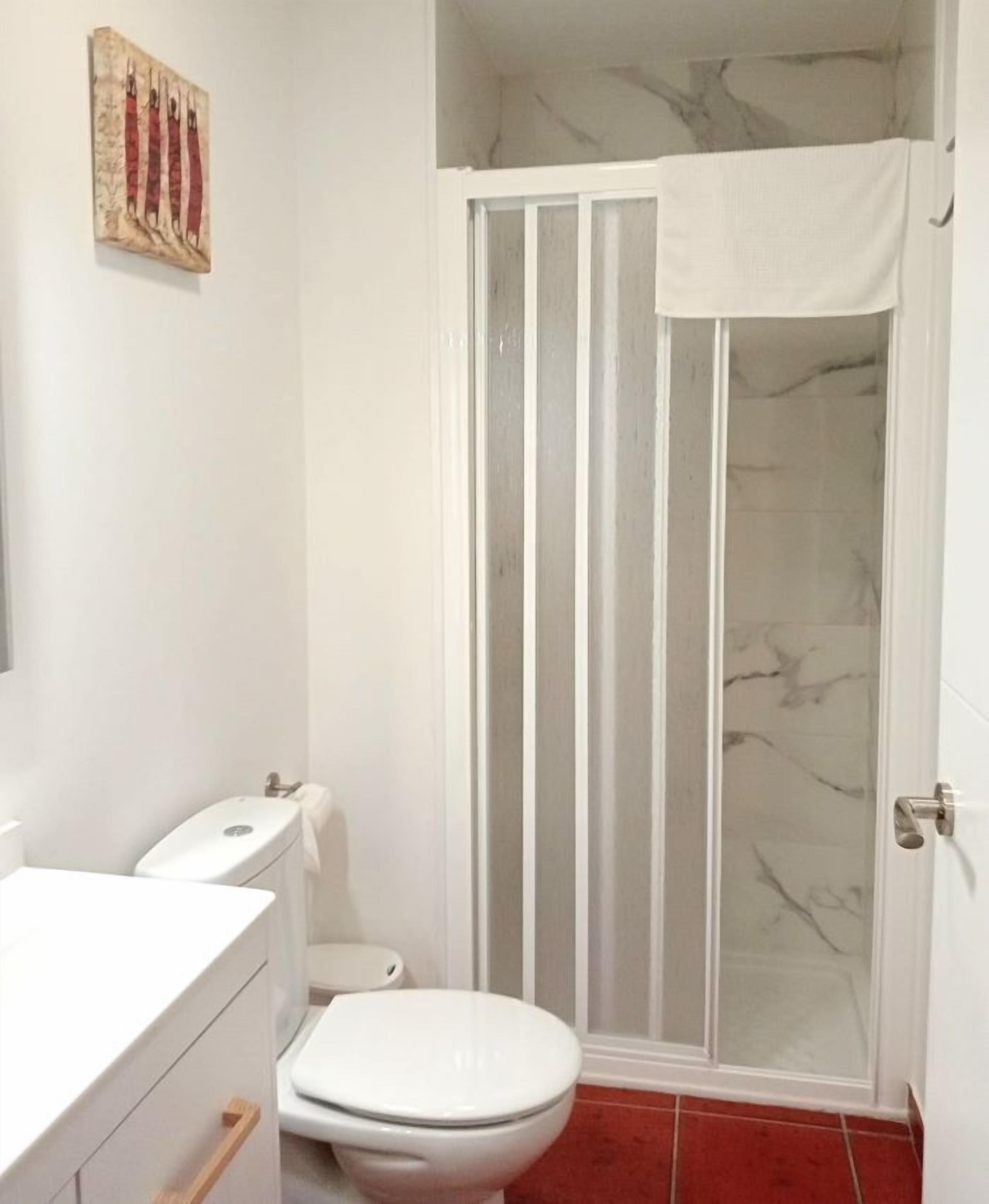 Ein Badezimmer mit Toilette, Waschbecken und Duschkabine, alles in Weiß.