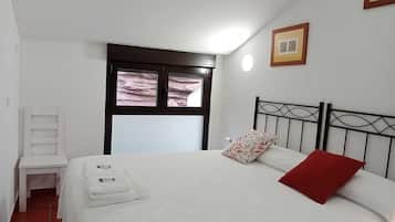 Un dormitorio con cama, una silla, un ventanal y un cuadro colgado en la pared.