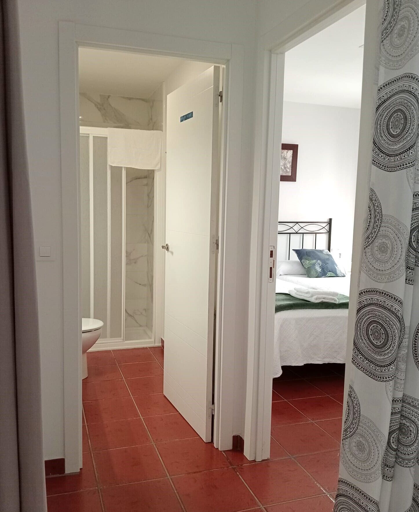 A hallway leading to a bathroom with a toilet and a shower.