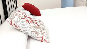 Una cama con un almohadón blanco con estampado de hojas y un almohadón rojo.