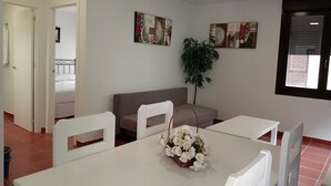 Una habitación de hotel con cama, sofá, mesa de comedor y sillas, y dos obras de arte colgadas en la pared.