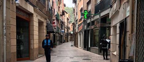 A narrow street with buildings on either side, featuring a patterned pavement and a few pedestrians.