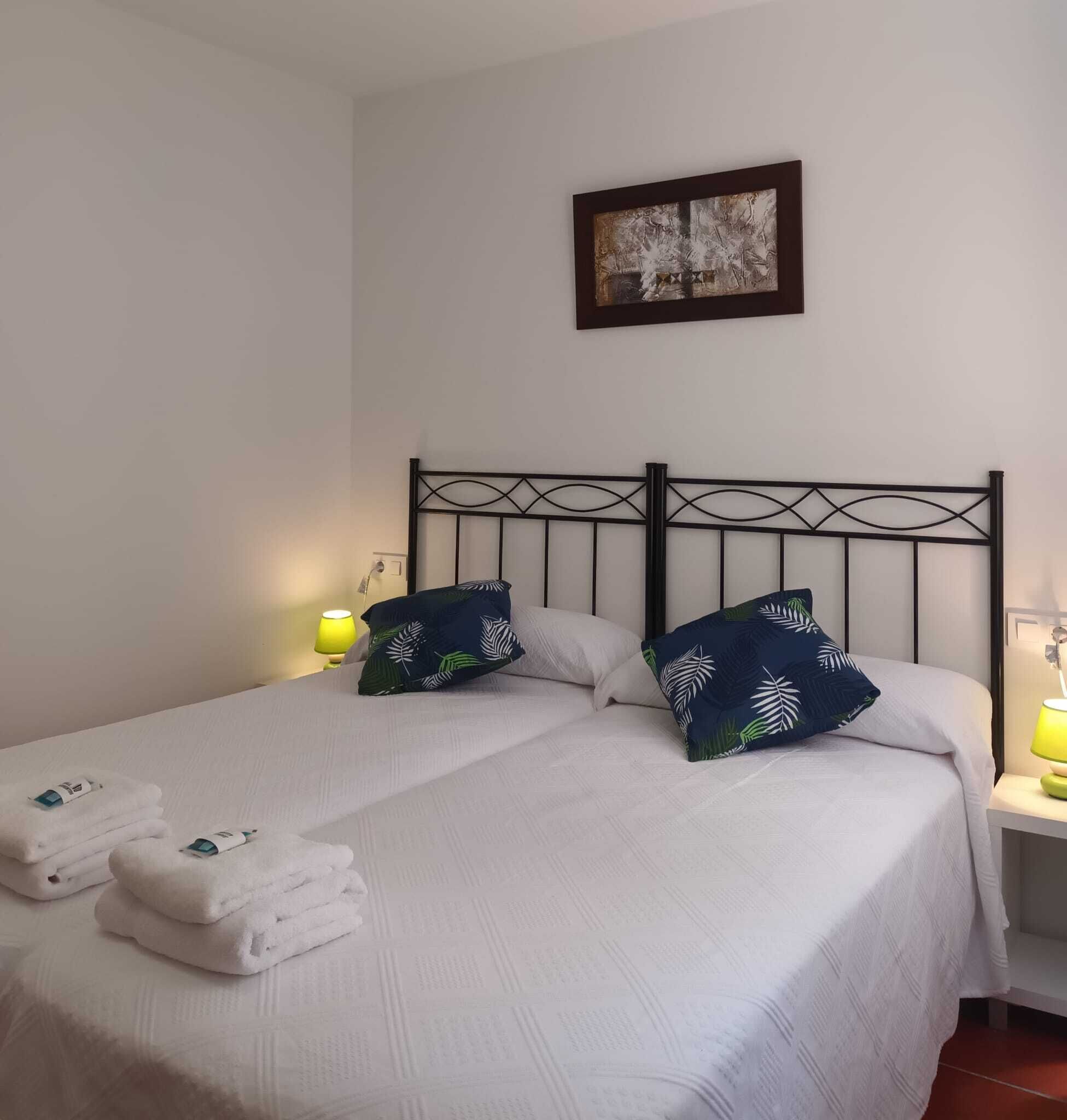A double bed with white linens, two pillows with a leaf pattern, and a framed artwork above.