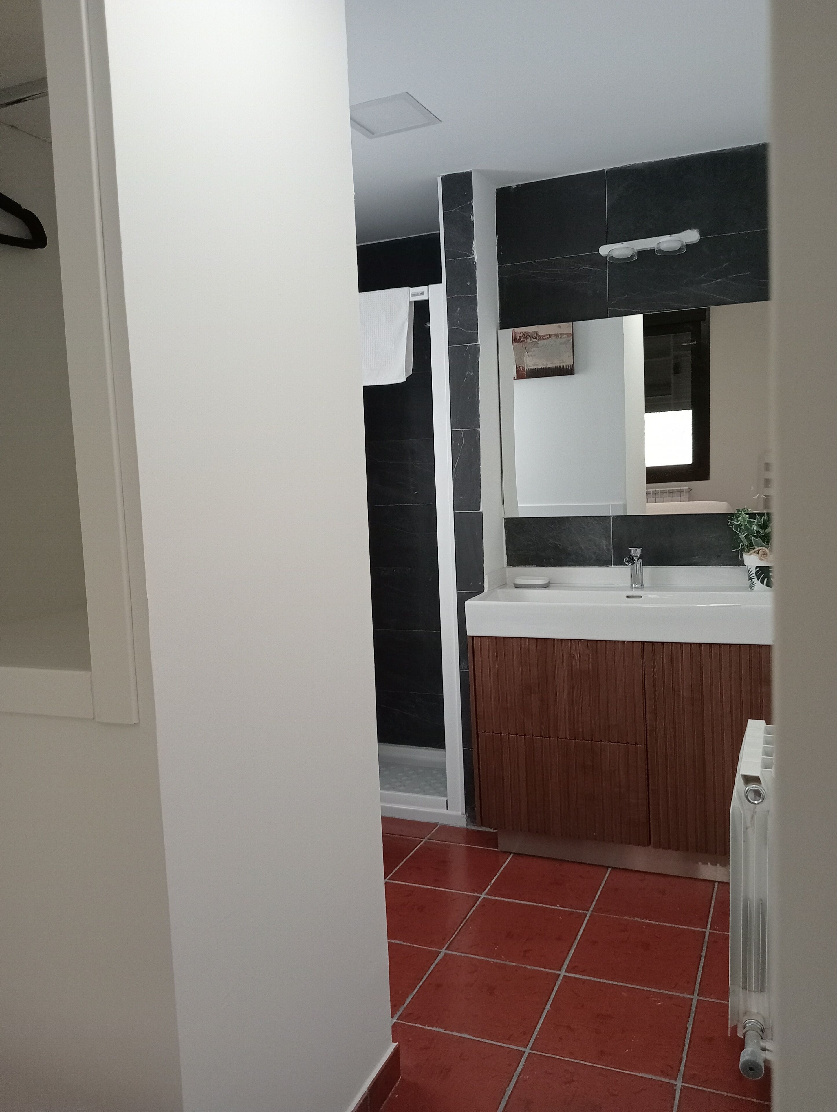 Un baño con lavamanos blanco, baldosas oscuras y tocador de madera.